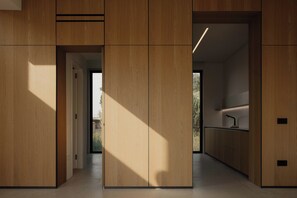 A modern interior with wooden paneling, a kitchen area with a sink, and a view through an open door. - The Habitus Project (Kerkira)