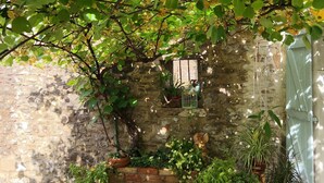 Un mur de pierres avec des plantes en pot, un banc en bois et une porte rustique.