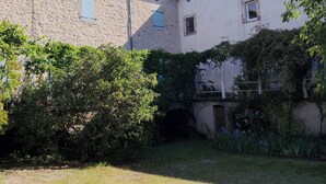 Une cour bordée de bâtiments en pierre, un petit pont et une végétation luxuriante.