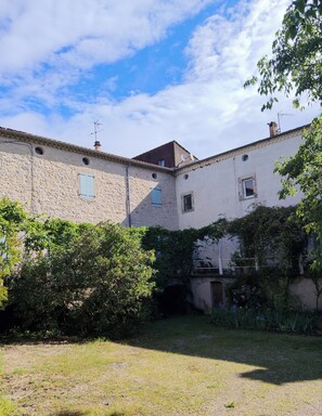 A courtyard with stone buildings, a small bridge, and lush greenery. - The serenity effect (Saint-André-de-Cruzières)