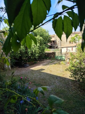 Um jardim com um muro de pedra, área gramada e um edifício com telhado de azulejos.