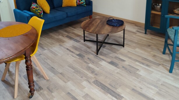 Un salon avec un canapé bleu, une table basse en bois, un fauteuil jaune, une lampe et un petit meuble.