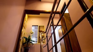 A staircase with a handrail, a potted plant, and a window with blinds. - Anandam Homestay (Ujjain)