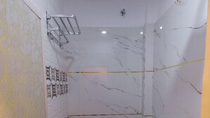 A small bathroom with a toilet, a shower, and a towel rack. - Anandam Homestay (Ujjain)