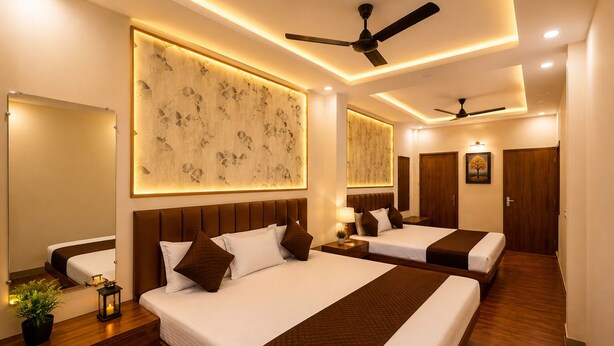 A hotel room with two beds, a ceiling fan, wall-mounted artwork, and a bedside table with a lamp and a plant. - Anandam Homestay (Ujjain)