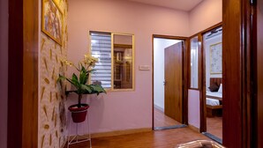 A hallway with a wooden floor, a potted plant, a framed picture on the wall, and a door leading to a bedroom. - Anandam Homestay (Ujjain)