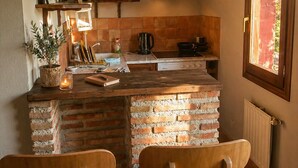 A kitchen with a brick island, wooden chairs, a window with a view, and a hanging light fixture.