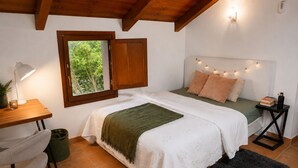 A bedroom with a bed, bedside table, lamp, window, and a view of greenery.