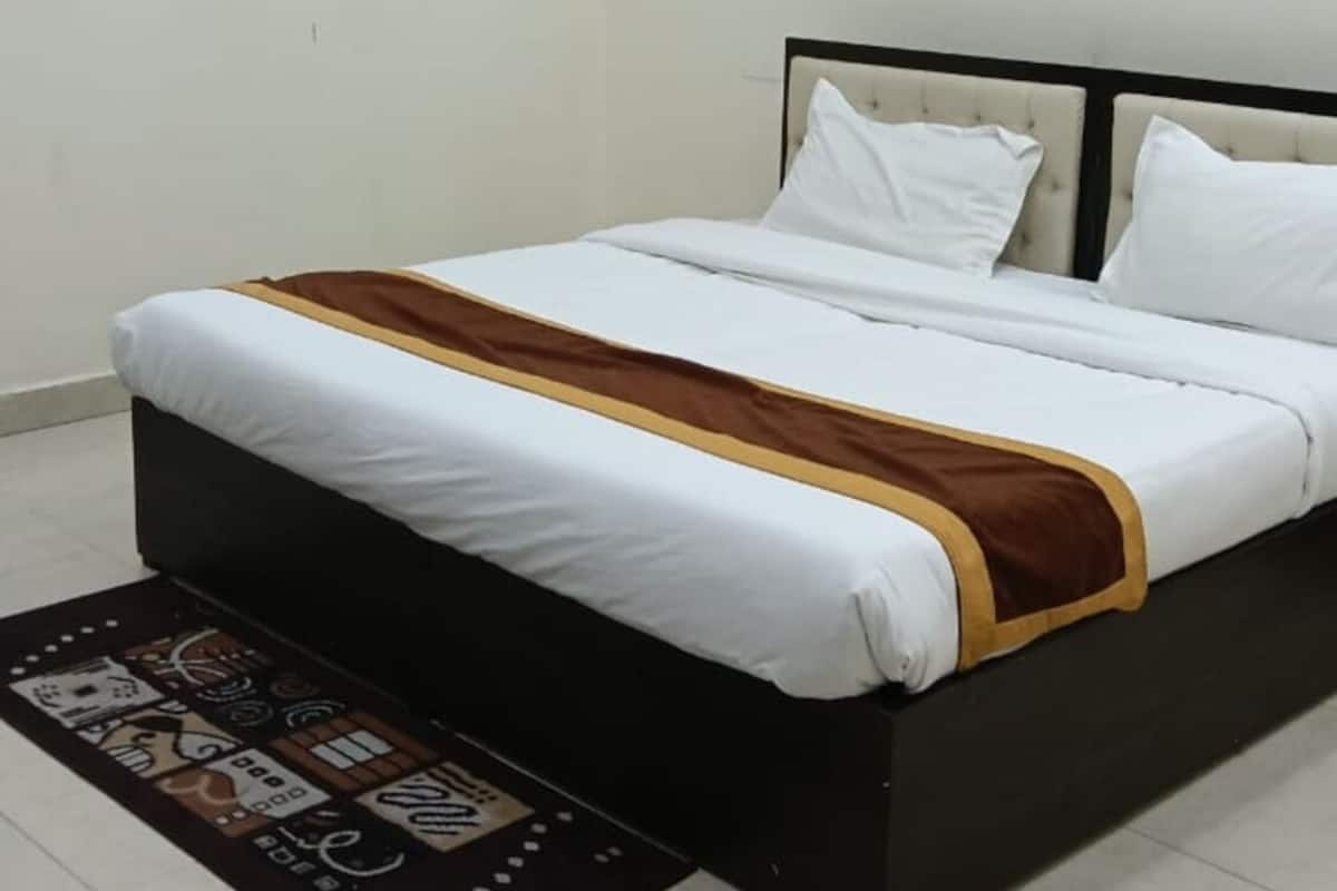 Quarto com cama, ar condicionado fixado na parede, quadro emoldurado e tapete estampado.