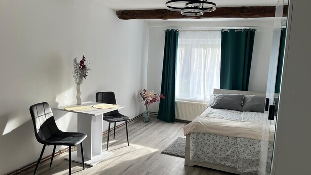 A modern bedroom with a bed, a small table, two chairs, a vase with flowers, and a window with curtains. - Cozy forest house / Przytulna Chatka w Lesie (Mątki)