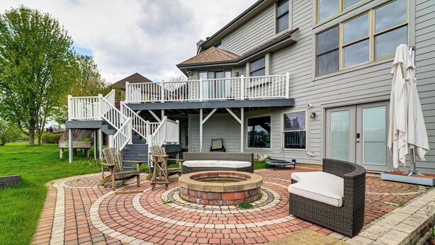 Casa de dos pisos con un patio que incluye un hogar circular, mobiliario exterior y una escalera que conduce a un balcón.