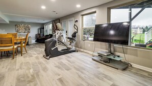 Un gimnasio en casa con equipo de ejercicio, un comedor y un televisor grande.