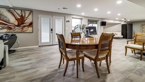 Un comedor con una mesa y sillas de madera, una silla de masaje y un cuadro abstracto grande en la pared.