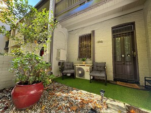 Un patio con una planta en maceta, dos sillas, una mesita y una puerta con un felpudo que dice 'Welcome'.