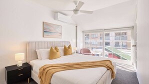 A hotel room with a bed, bedside table, lamp, ceiling fan, window, and artwork on the wall. - Harris St House | 5 Mins to Darling Harbour & CBD (Pyrmont)