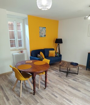 Un salon avec une table ronde en bois, des chaises jaunes, un canapé bleu, un lampadaire et un radiateur.