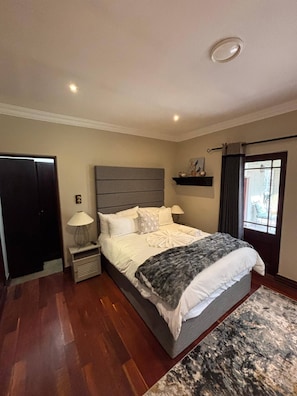 Een slaapkamer met een groot bed, nachtkastjes, een raam met gordijnen en een deur.