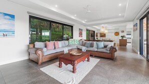 A spacious living area with a large sectional sofa, a wooden coffee table, and a view of greenery through large windows.