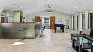 A spacious indoor area with a pool table, a bar area, and a seating area with a sofa and chairs.