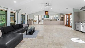 A spacious living area with a black leather sofa, a glass coffee table, and a kitchen in the background.
