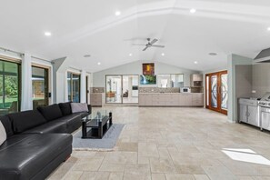 A spacious living area with a black leather sofa, a glass coffee table, and a kitchen in the background. - Ultimate 5BR Luxury Estate Family & Group Haven (Capalaba)