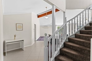 A staircase with white balusters leading to a landing, a white console table with a vase, and a framed picture on the wall. - Ultimate 5BR Luxury Estate Family & Group Haven (Capalaba)