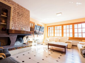Ein Wohnzimmer mit Kamin aus Stein, einem Fernseher, einer Couch und einem Couchtisch.