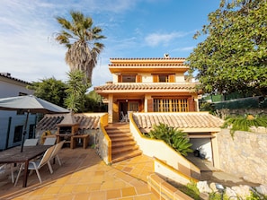 A two-story building with a tiled roof, a staircase leading to the entrance, and a patio area with outdoor furniture.
