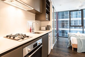 Eine moderne Küche mit Gasherd, Spüle und Toaster. Im angrenzenden Zimmer befindet sich ein Bett mit Decke und Kissen.