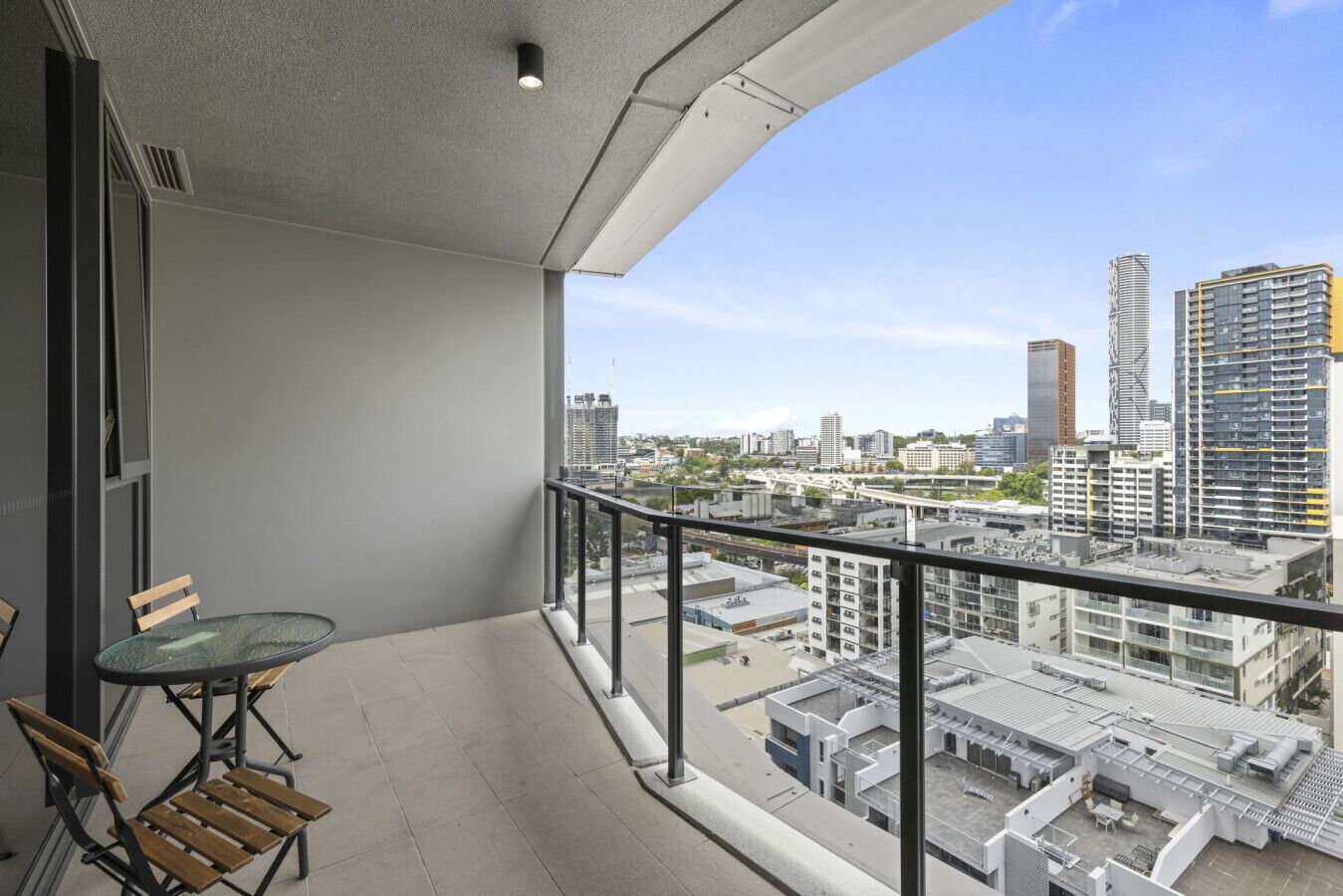 Un balcon avec une table et des chaises en verre, d’où l’on peut admirer un panorama sur la ville, avec ses différents bâtiments.