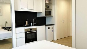 Une cuisine de taille réduite avec des meubles blancs, un plan de travail noir, un four à micro-ondes et un réfrigérateur.