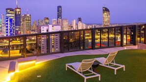 Une terrasse sur le toit, dotée de deux chaises longues, d’une rambarde en verre et offrant une vue panoramique sur la ville.