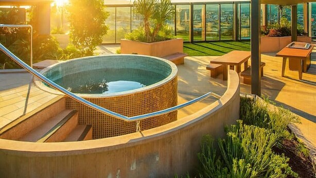 Un espace piscine sur le toit, avec un jacuzzi, des sièges extérieurs et une vue sur le paysage urbain.