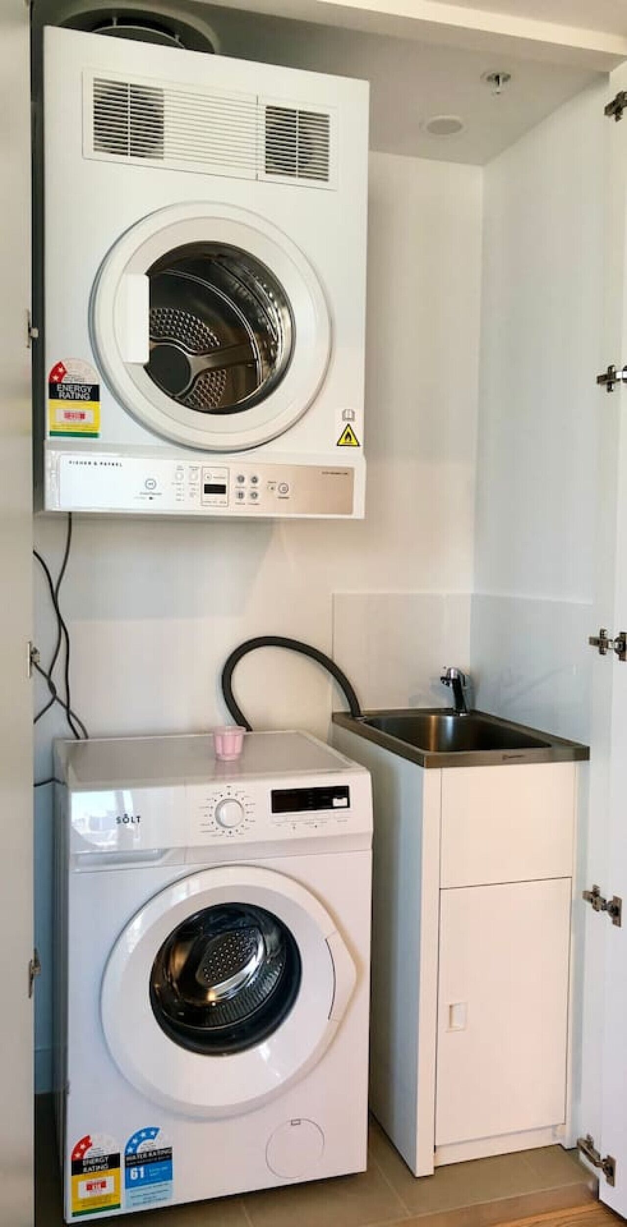 Ein kleiner Waschraum mit einer Waschmaschine und einem Trockner, einem Waschbecken und einem Schrank.