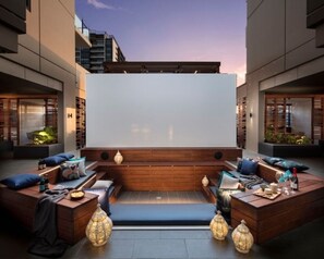 A rooftop terrace with a large screen, wooden seating, and ambient lighting. - Cultural Charm - 2BR Apartment in South Brisbane (South Brisbane)