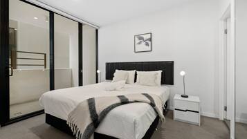 A modern bedroom with a large bed, a bedside table with a lamp, a sliding glass door, and a framed picture on the wall.