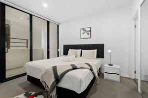 A modern bedroom with a large bed, a bedside table with a lamp, a sliding glass door, and a framed picture on the wall. - Cultural Charm - 2BR Apartment in South Brisbane (South Brisbane)