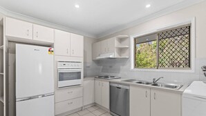 A modern kitchen with white cabinets, a built-in oven, a dishwasher, and a window with a view of greenery. - Cozy & Spacious 2-Bedroom Retreat (Capalaba)