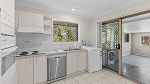 A modern kitchen with white cabinets, a dishwasher, a stove, and a window with a view of greenery. - Cozy & Spacious 2-Bedroom Retreat (Capalaba)
