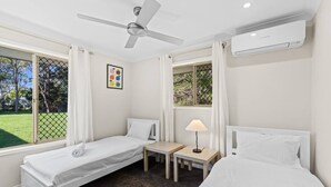 A room with two beds, a ceiling fan, an air conditioning unit, and a small table with a lamp. - Cozy & Spacious 2-Bedroom Retreat (Capalaba)