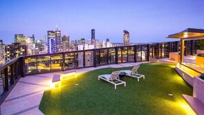 Una terraza en la azotea con vistas al horizonte de la ciudad, mobiliario exterior y zona bien iluminada.