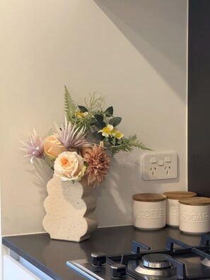 Eine Küchenarbeitsplatte mit einer dekorativen Blumenvase, einem Gaskochfeld und beschrifteten Behältern für Kaffee und Zucker.