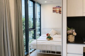 Ein Schlafzimmer mit Bett, Fenster, einem Teddybären und einer Blumenvase.