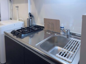 Uma cozinha com fogão a gás, pia de aço inoxidável e bancada branca.