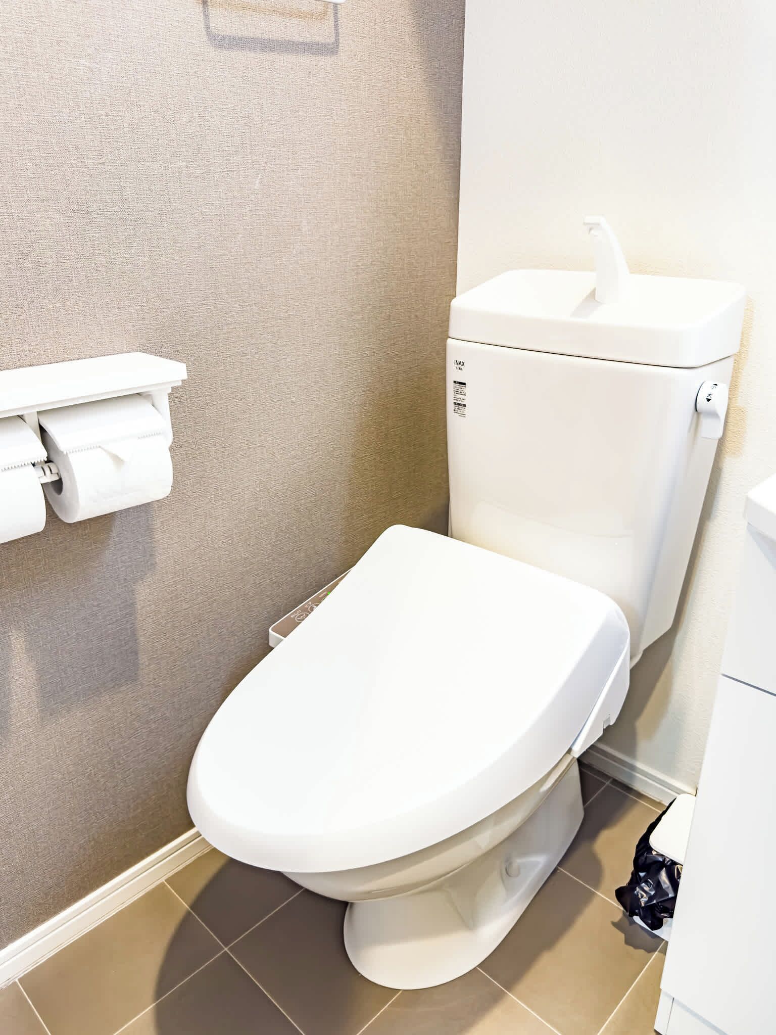 Eine weiße Toilette mit Tank, Toilettenpapierhalter und einem an der Wand befestigten Spülknopf.