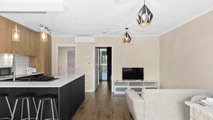 A modern kitchen with a central island, bar stools, a dining area with a sofa, and a TV on a stand. - Modern Tropical 1BR Oasis in Spring Hill (Spring Hill)
