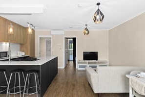 Eine moderne Küche mit einer zentralen Kochinsel, Barhocker, einem Essbereich mit einer Couch und einem Fernseher auf einem Schrank.