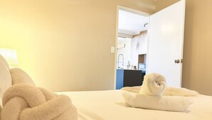 A hotel room with a bed, a rolled towel on the bed, and a view of a bathroom and kitchenette in the background. - Modern Tropical 1BR Oasis in Spring Hill (Spring Hill)