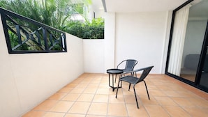 Un petit espace patio doté d’un sol carrelé, de deux chaises, d’une petite table, d’une rambarde en métal et d’une porte-fenêtre coulissante.