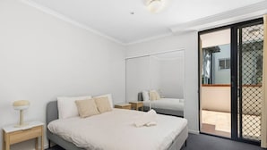 Une chambre à coucher comprenant un lit, des tables de chevet, un miroir et une porte-fenêtre coulissante donnant sur un espace extérieur.